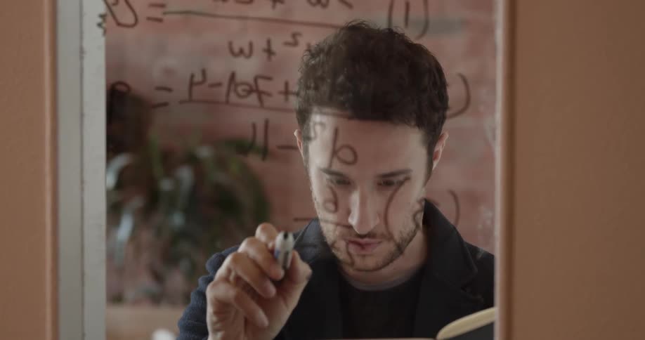 A man writes math equations on a window