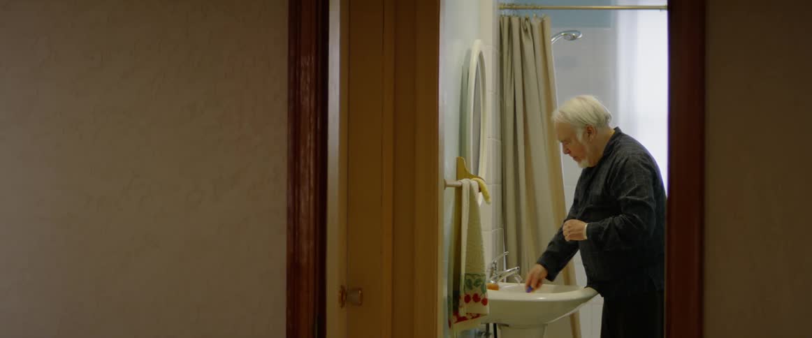 Elderly man shaves as he looks in a bathroom mirror