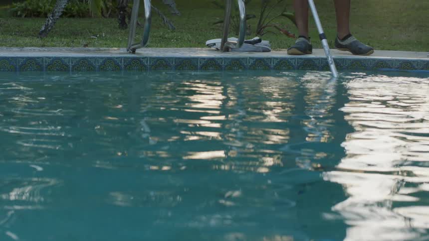 Man vacuums a swimming pool as he stands at the edge of it