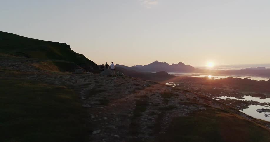 People stand on the hill as the sun sets over the lake