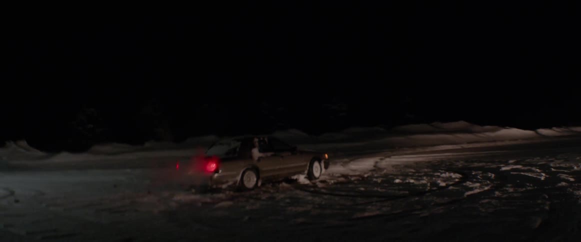 A car is driving in a vacant lot at night in winter