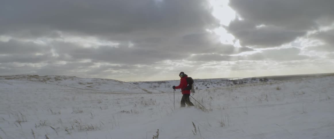 The man is hiking through the snow with sticks