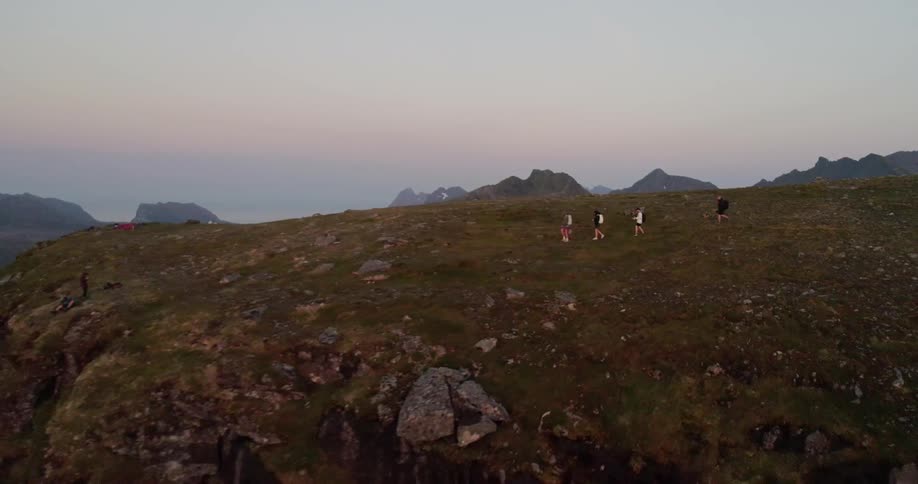 A group of people is hiking toward a cliff in a natural landscape at dusk