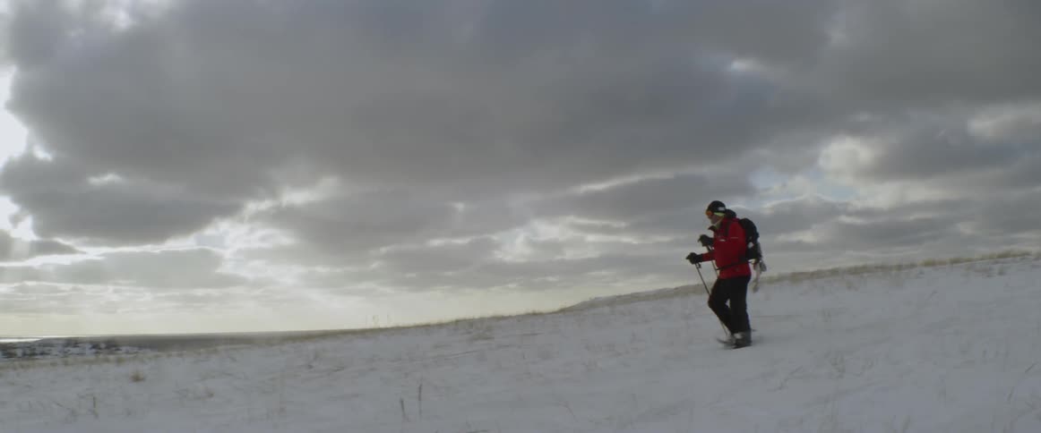 Person hikes through a snowy field using ski poles