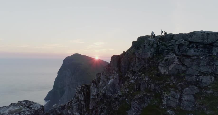Hikers stand on the edge of a cliff looking at the sunset