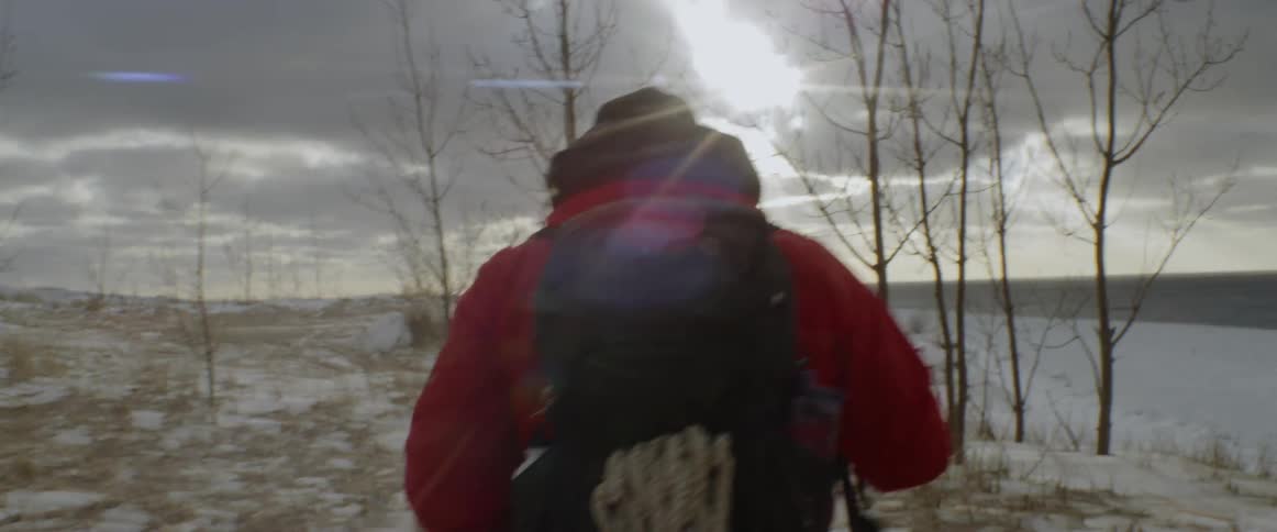 A man is trekking across a snow-covered landscape toward the coast in daylight