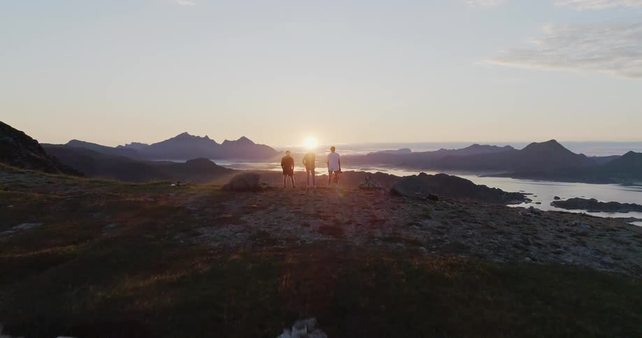 People stand on the edge of a cliff at sunset