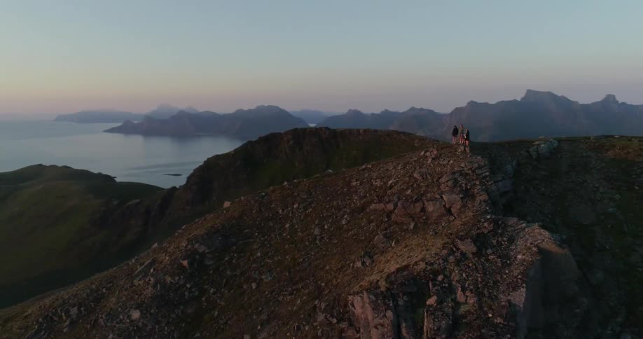 Hikers stand on a mountain peak at sunset