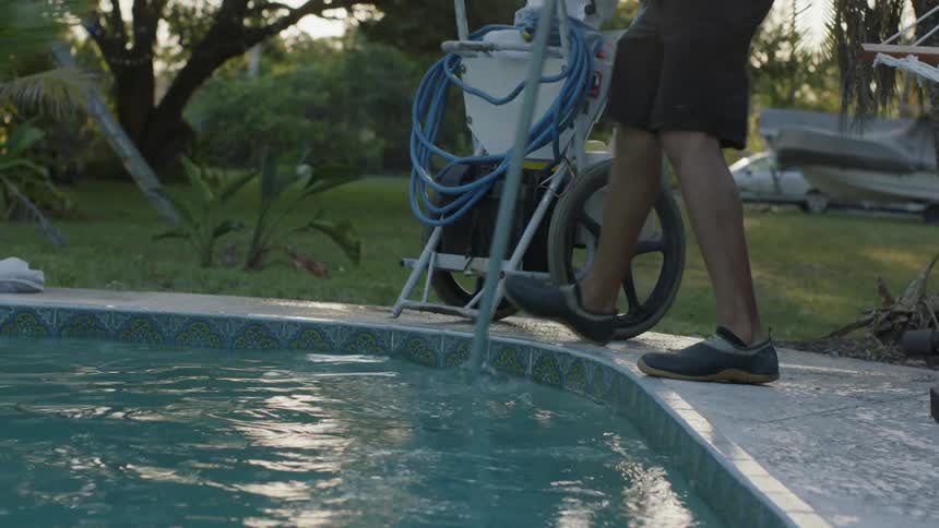 A man is cleaning a pool in a yard in daylight