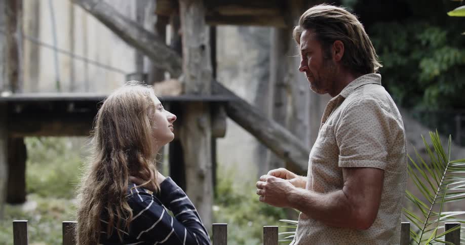 A man is explaining something to his daughter as they stand outside an exhibit at a zoo