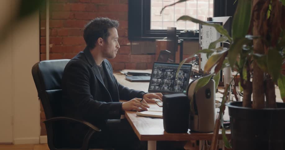 Man sits at a desk and writes in a notebook then looks at a monitor