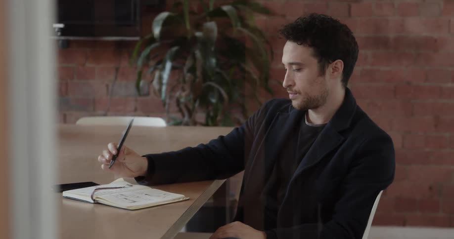 A man is sitting at the table tapping his notebook