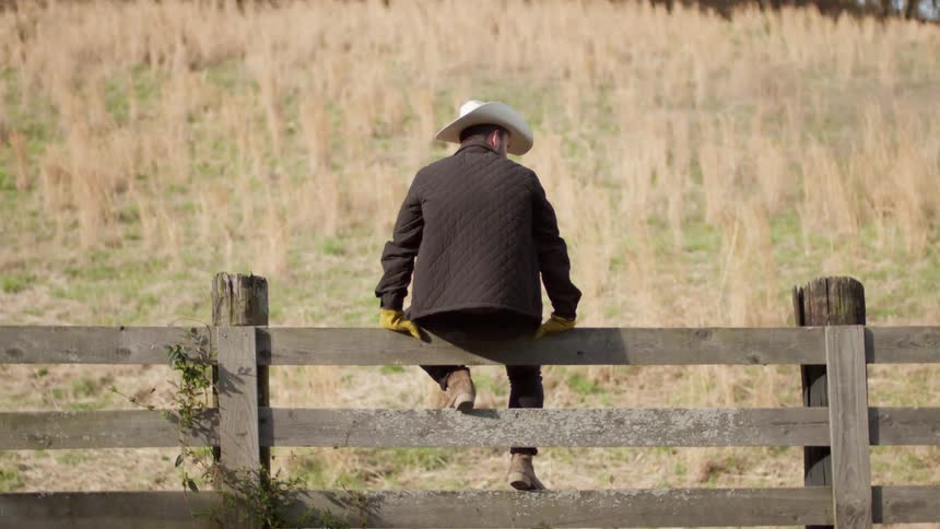 A man sits on the fence near the farm