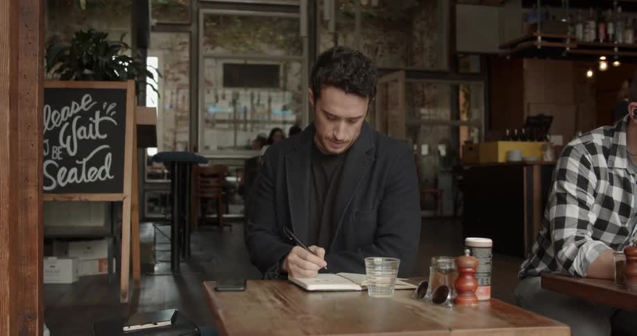A man writes in a notebook in a coffee shop