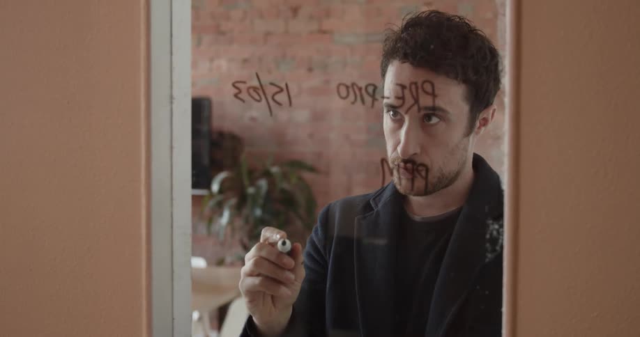 A man writes on glass with a dry erase marker
