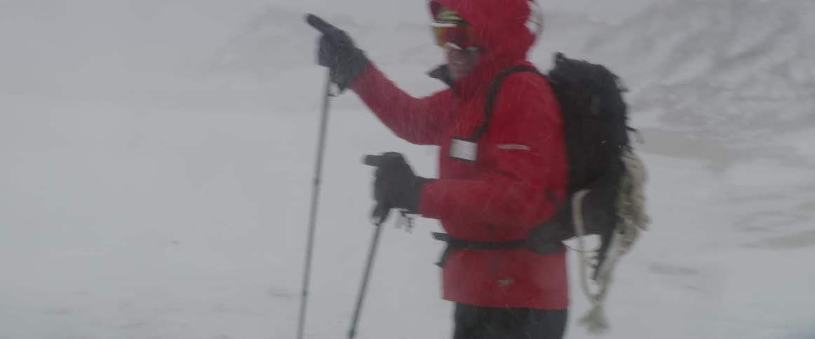 A man is pointing toward a direction as he stands in a remote area in a blizzard