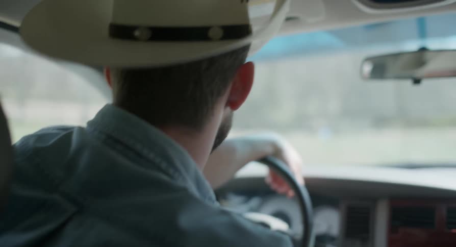 A man in a cowboy hat is driving a car