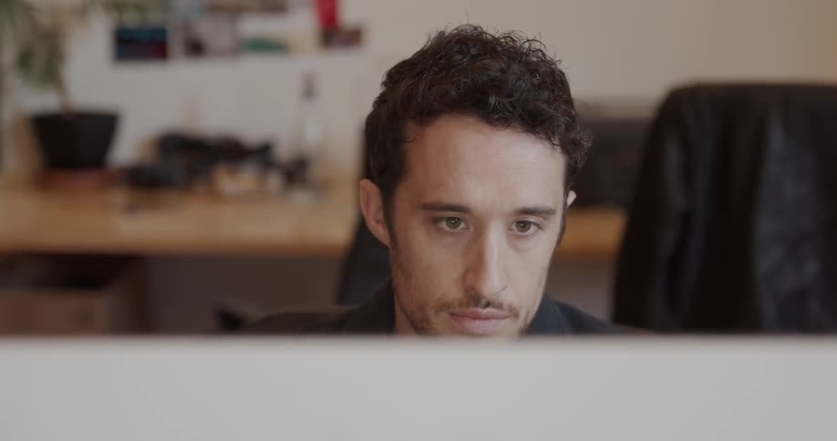 Man sits at a desk looking at a computer monitor