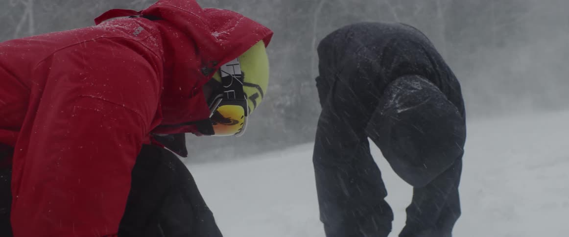 Two people standing in the snow adjust their skis