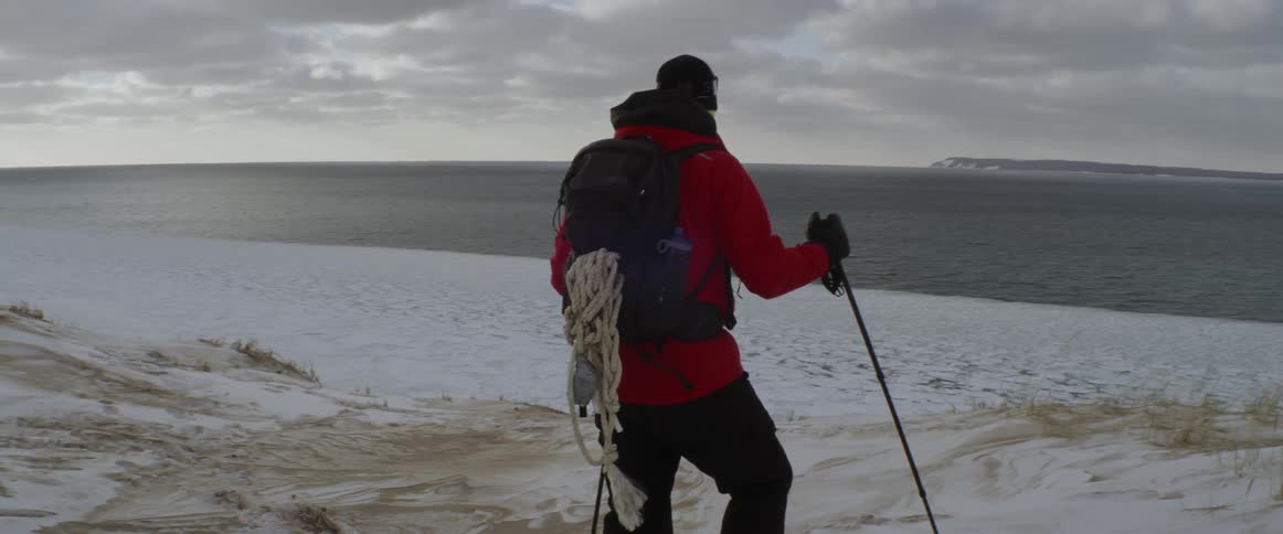 Man wearing a backpack leaning on a pole looks out at the water