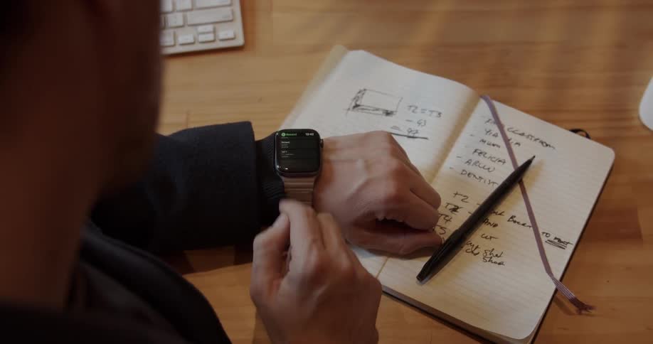 A man checks his watch and writes in a notebook
