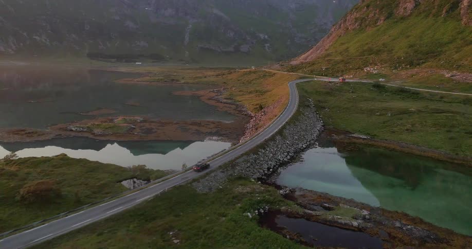 A car drives on a rural mountain road at sunset