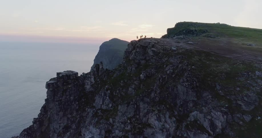 People stand on the edge of a cliff overlooking the ocean at sunset