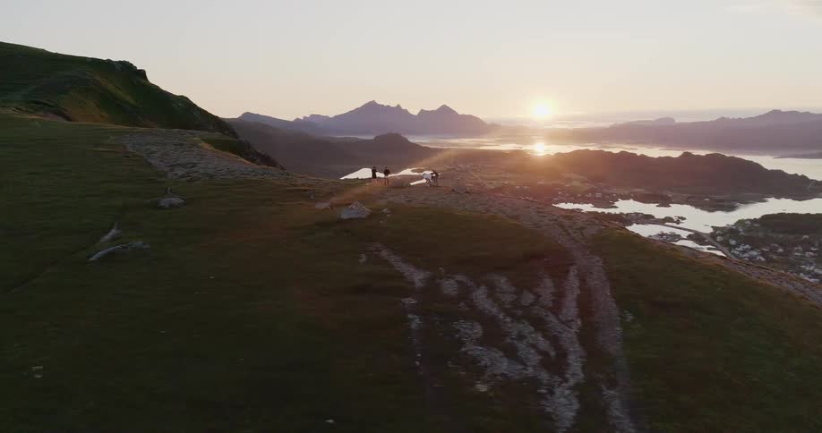 The people stand on the edge of a cliff overlooking the sunset near the shore