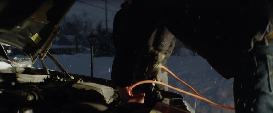 Two men attempt to jump start a car as it snows