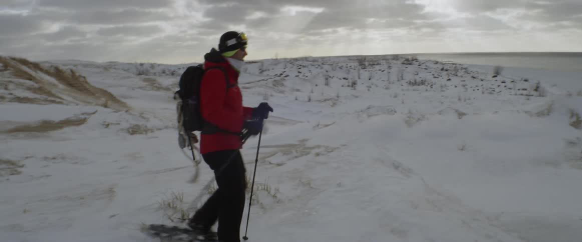 A man is hiking with sticks and snow shoes