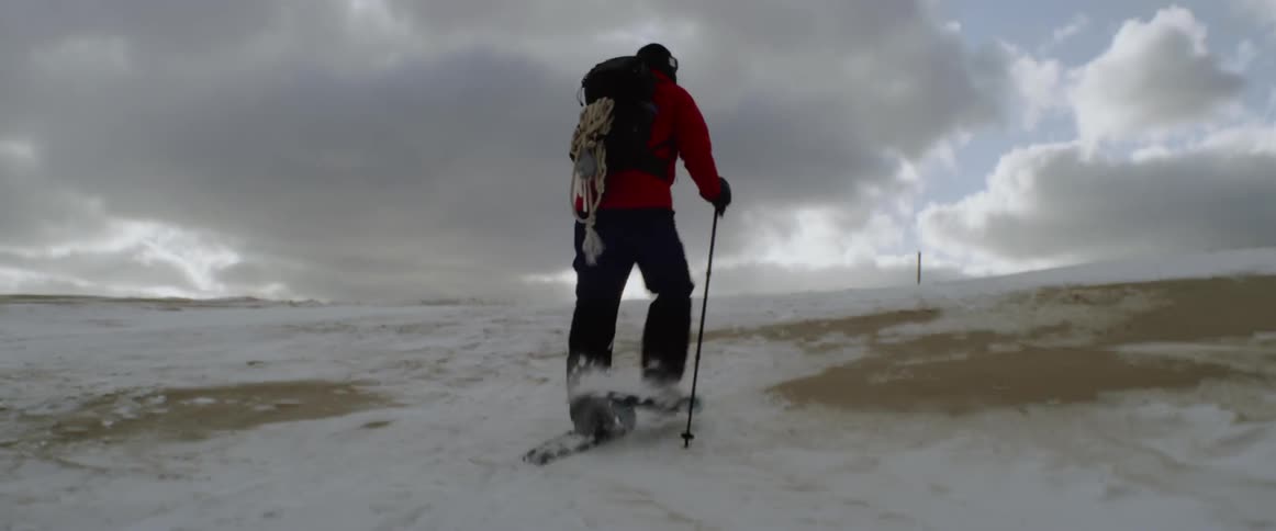 A man climbs a snowy hill with skis