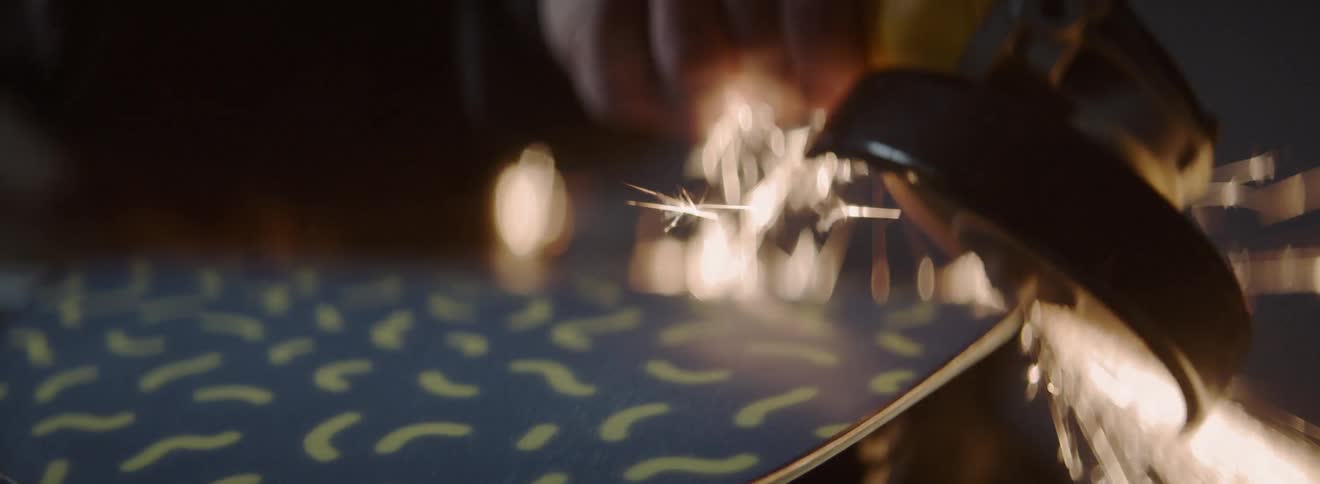 A man is grinding down the edge of a snowboard with a grinder inside in daylight