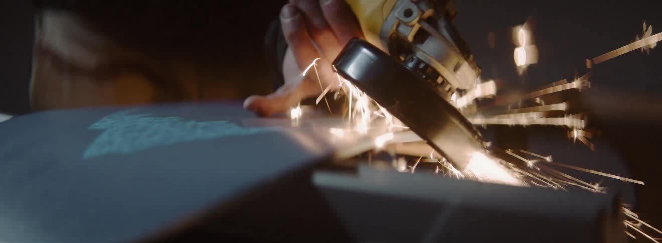 A person wearing a safety mask using a tool to cut glass with sparks flying