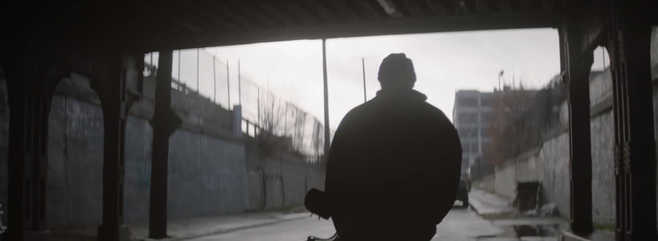 A man is carrying a snowboard as he walks down an urban street on a cloudy day