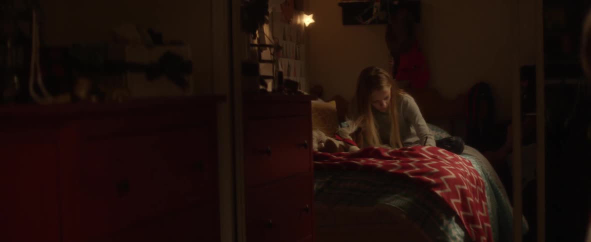 Reflection of a girl writing on a bed as a woman walks over next to her