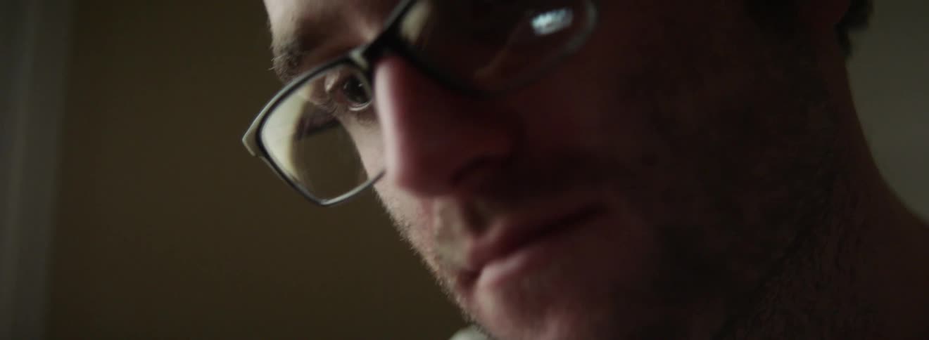 A man wearing glasses looks down at a monitor which is reflected in the lens