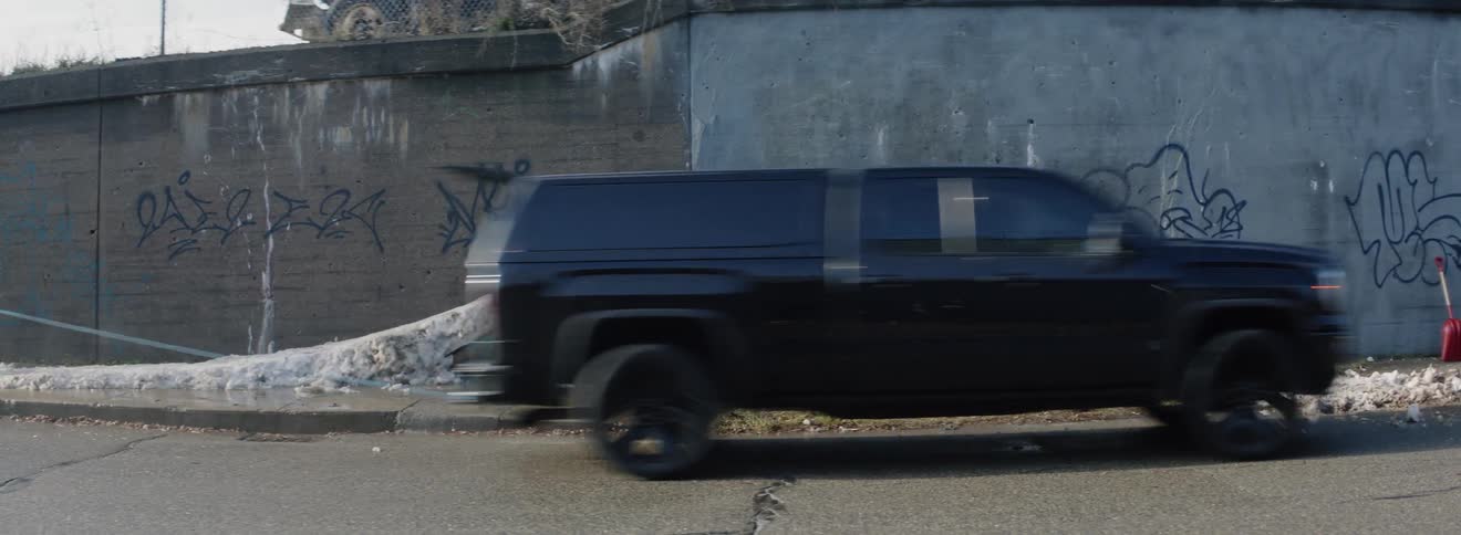 The car drives by as a person snowboards off the brick wall