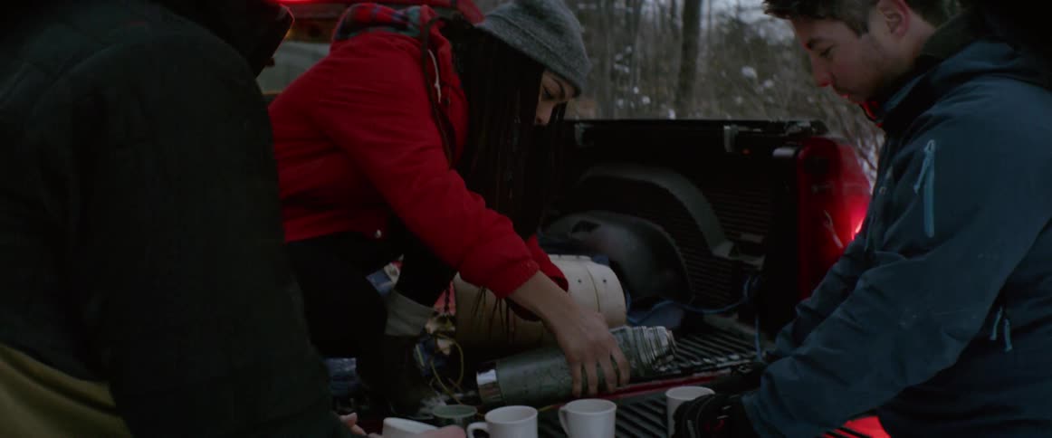 Woman in the back of a pickup truck pours coffee from a thermos into a mug