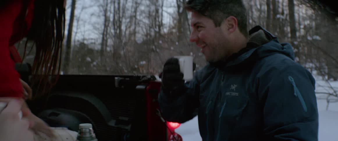 Friends are drinking cups of hot cocoa as they stand at a pickup truck outside on a winter morning