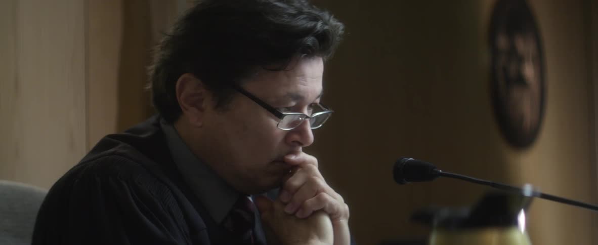 Man adjusts his glasses and puts his hands to his chin
