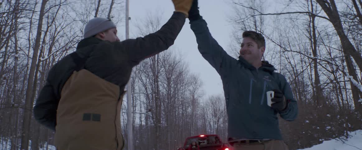 A man runs to the truck to pull a man on a snowboard