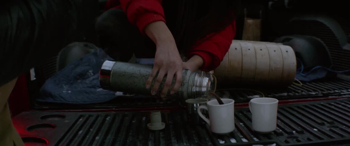 A woman pours hot cocoa from a thermos while sitting in a truck bed with friends