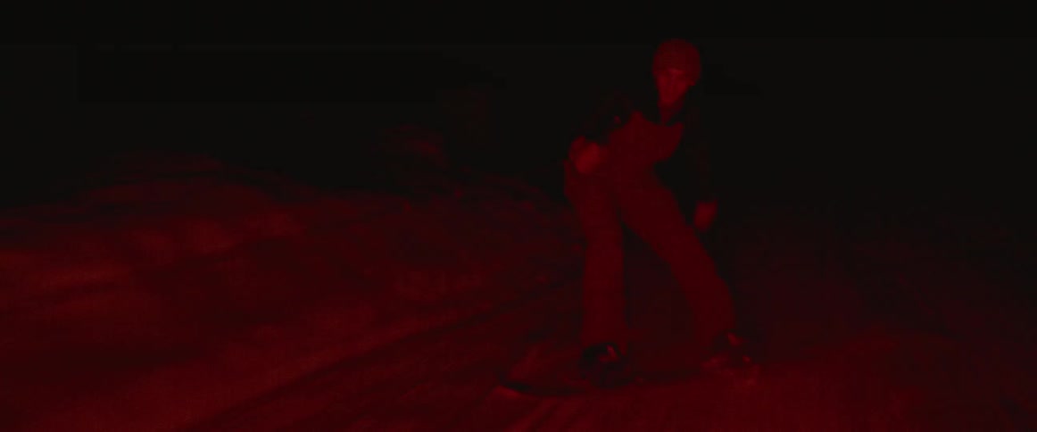 A young man holds onto a cable as he snowboards behind a moving vehicle at night, falling and getting back up