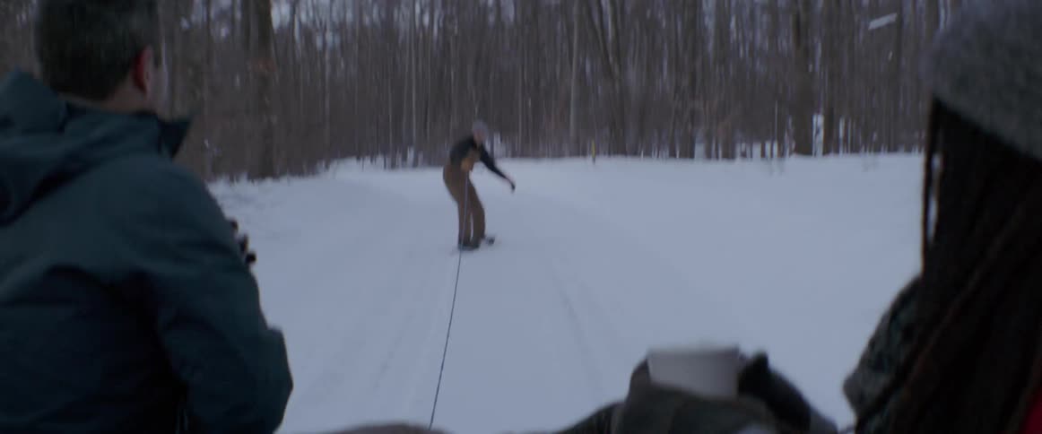 The man is riding his snowboard being pulled by a truck