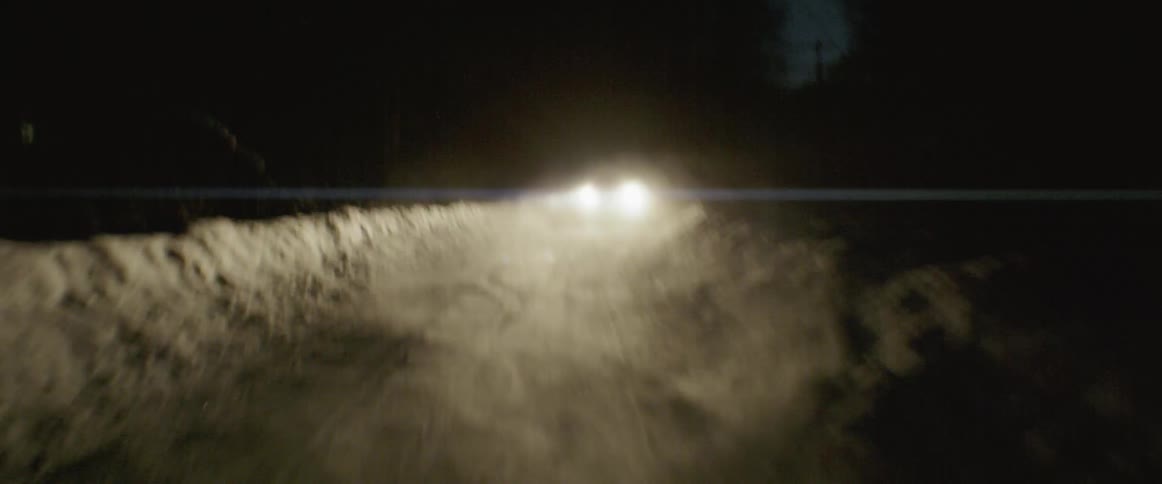 A vehicle is kicking up snow behind it as it drives down a road at night