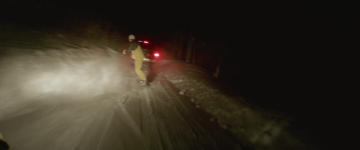 Person balancing on a snowboard being pulled by a truck at night
