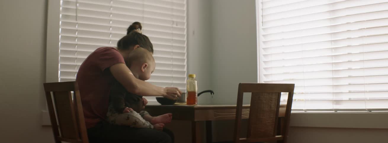 A baby is being fed at the table by a woman