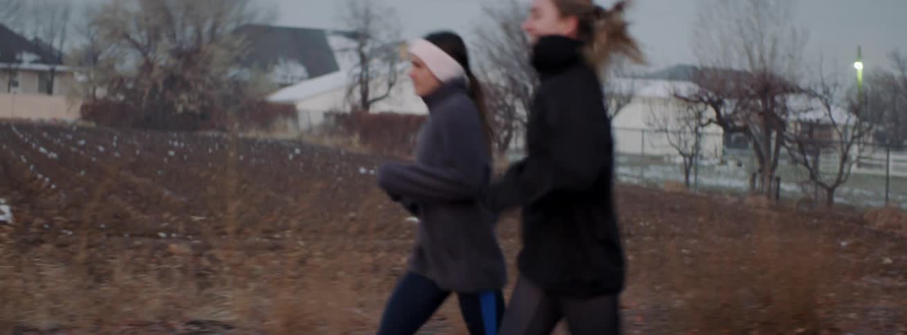 Two women jog on a sidewalk in the cold