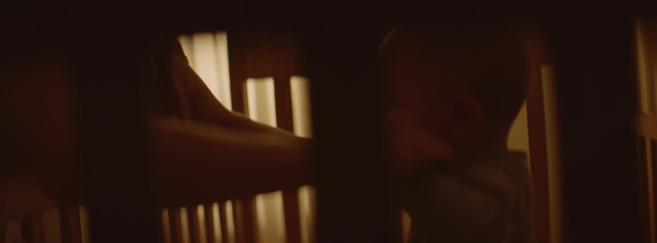 Woman lifts baby by his hands while he is in his crib