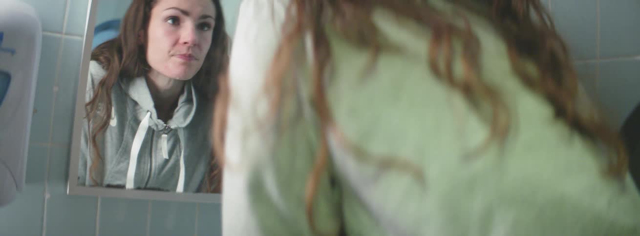 A woman splashes water on her face as she looks in a mirror
